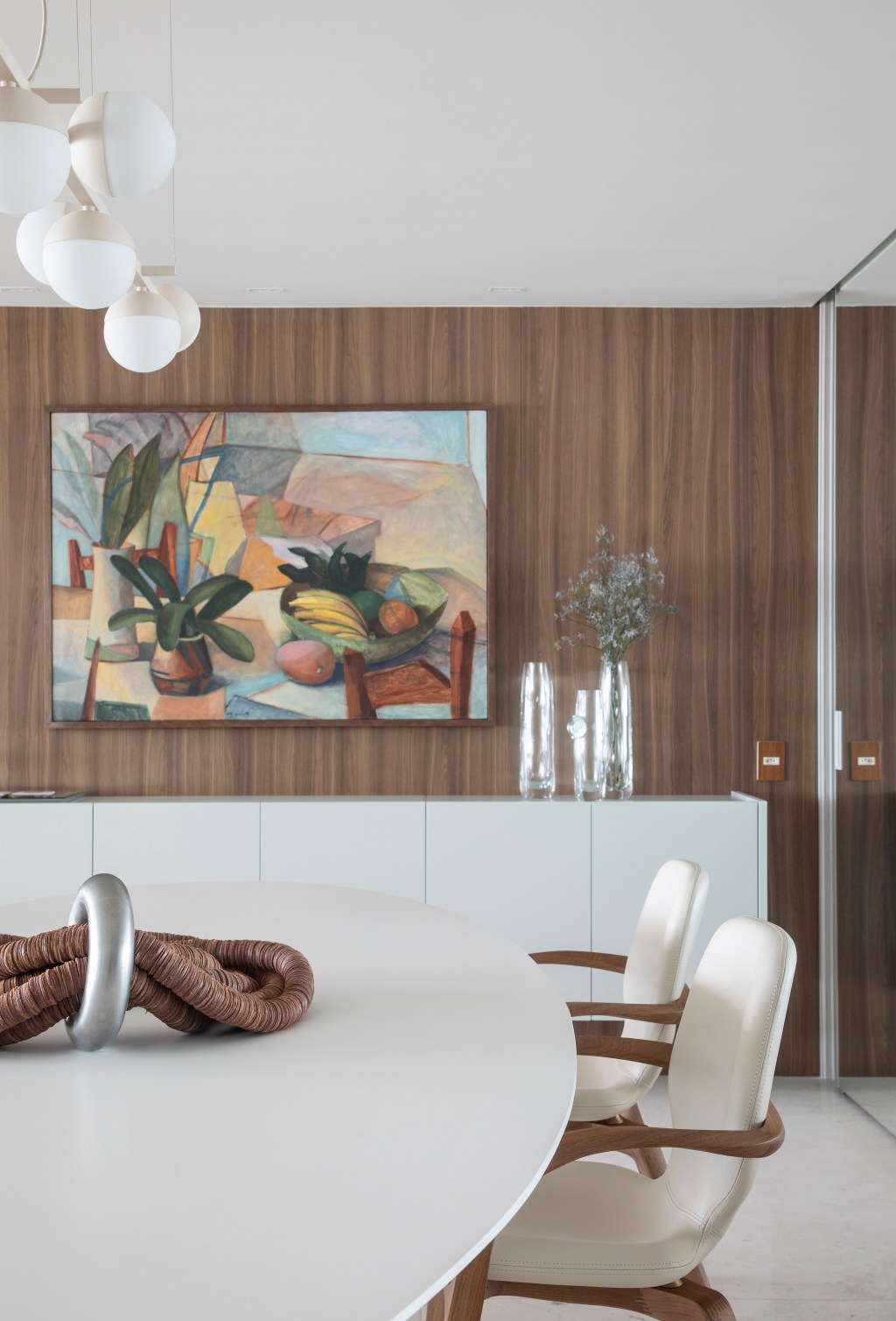 Décor de apê de 200 m² valoriza a vista do mar e obras de arte da moradora. Projeto de Ana Moura Ana Higino Arquitetura. Na foto, sala de jantar com parede de madeira, quadro e mesa branca.