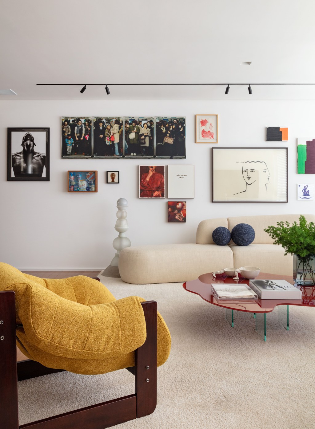 Obras de arte e móveis de design marcam o apê de colecionador. Projeto de Nop Arquitetura. Na foto, sala de estar com quadros, sofá curvo e poltrona.