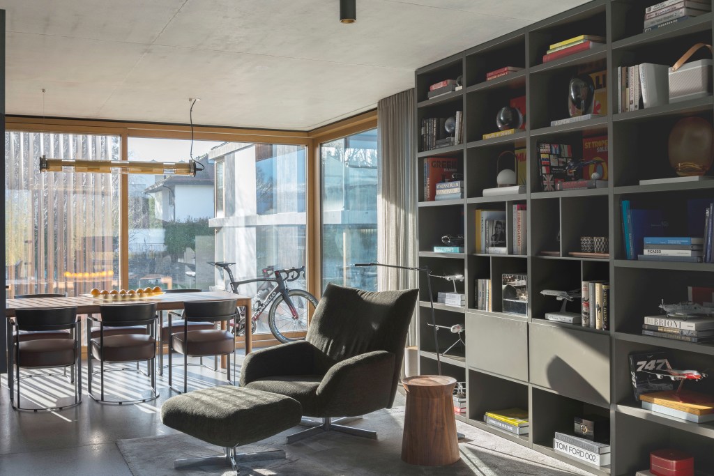 David Bastos projeta apartamento na Suíça repleto de design assinado. Na foto, sala com mesa de jantar, estante e poltrona de leitura.