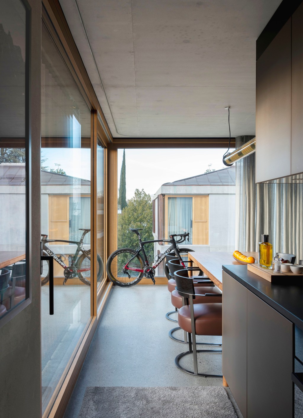 David Bastos projeta apartamento na Suíça repleto de design assinado. Na foto, cozinha com parede de vidro, bancada e bicicleta.