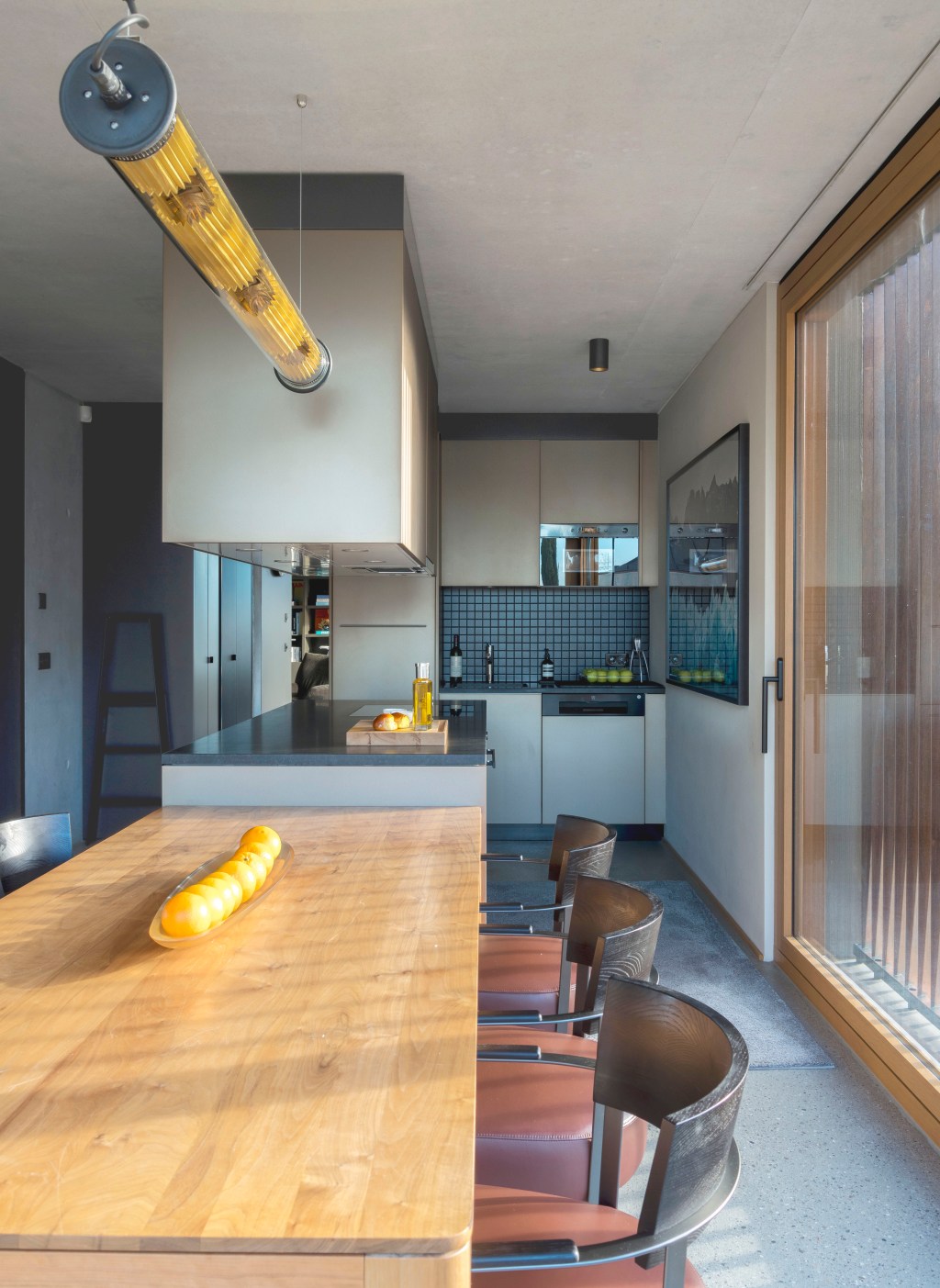 David Bastos projeta apartamento na Suíça repleto de design assinado. Na foto, cozinha com bancada, mesa e armários suspensos.