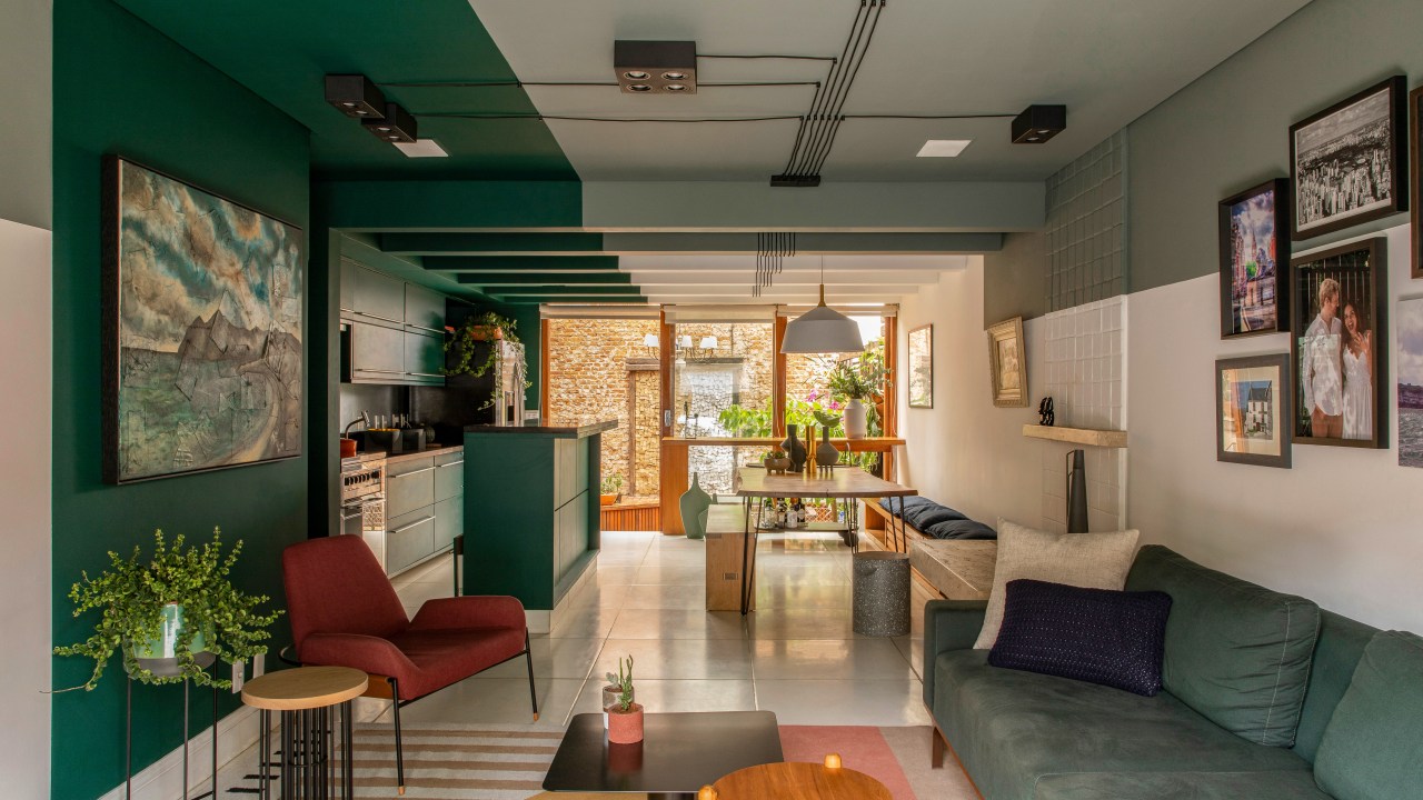 Degradê de tons de verde setoriza esta casa de vila em São Paulo. Projeto de Ricardo Abreu. Na foto, sala e cozinha com paredes verdes, sofá e quadros.