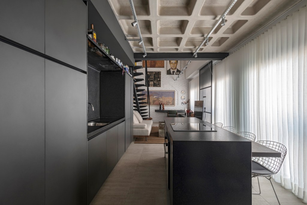 Loft de 64 m² ganha décor industrial e coleção de arte dos moradores. Projeto de Junior Piacesi. Na foto, cozinha com ilha e marcenaria preta.