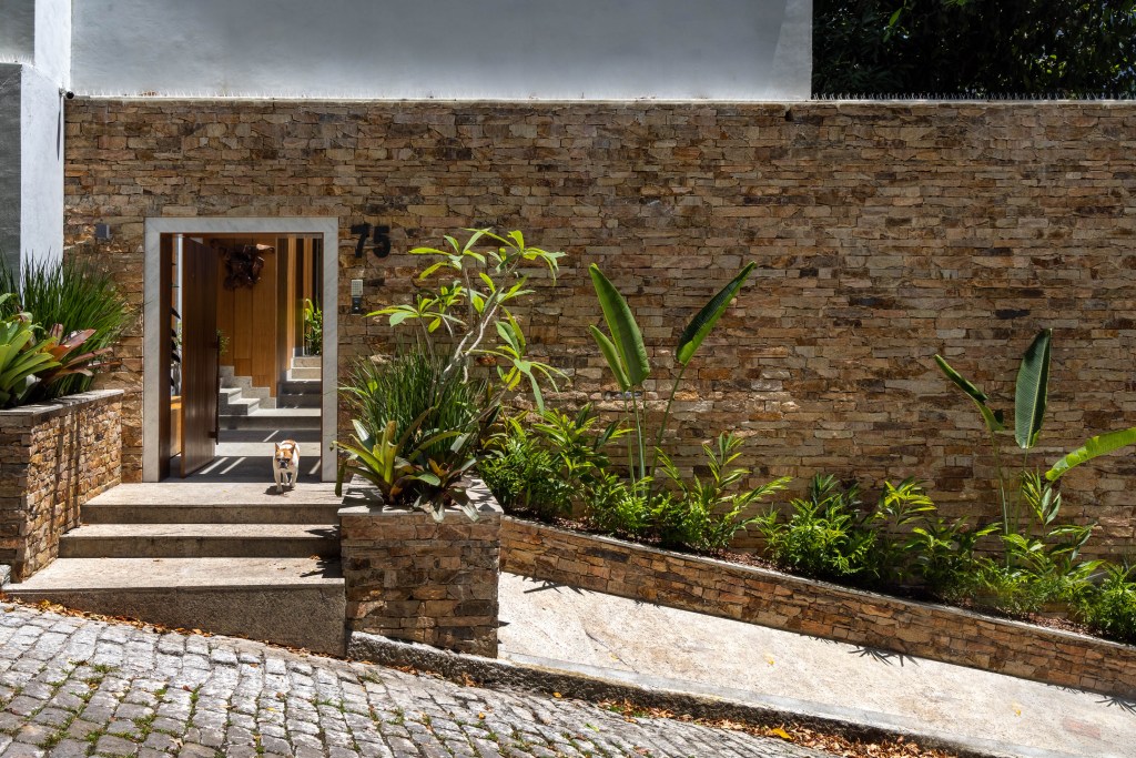 Triplex tem estúdio de música, entrada privativa da rua e vista para Lagoa, Projeto Maurício Nóbrega. Na foto, entrada privativa com muro de pedra e paisagismo.