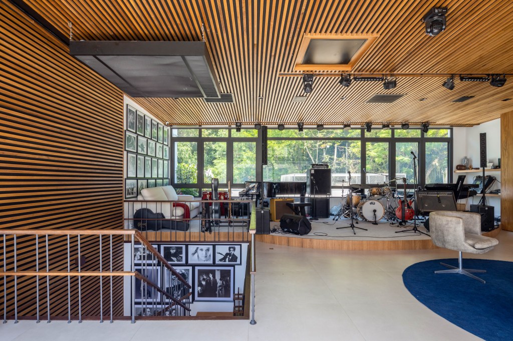Triplex tem estúdio de música, entrada privativa da rua e vista para Lagoa, Projeto Maurício Nóbrega. Na foto, escada com quadros. Estúdio de música com teto ripado de madeira, instrumentos e vista para a natureza.