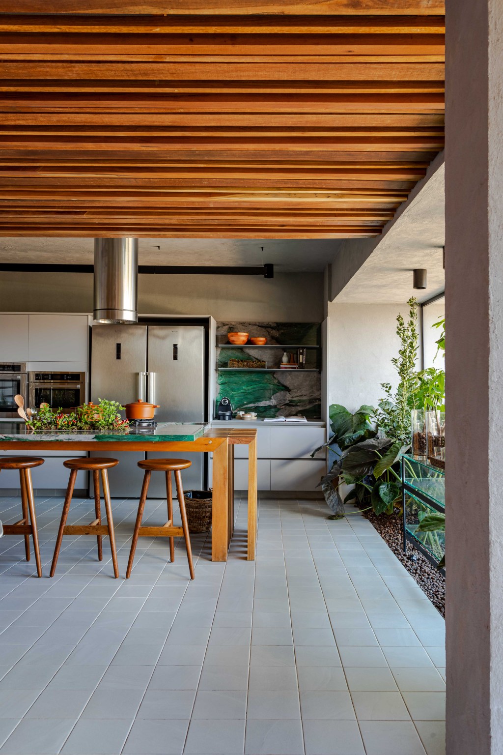 Cozinha Ágape, projeto de Tatiana Melo para a CASACOR Bahia 2023. Na foto, cozinha com ilha, jardim e teto de madeira.