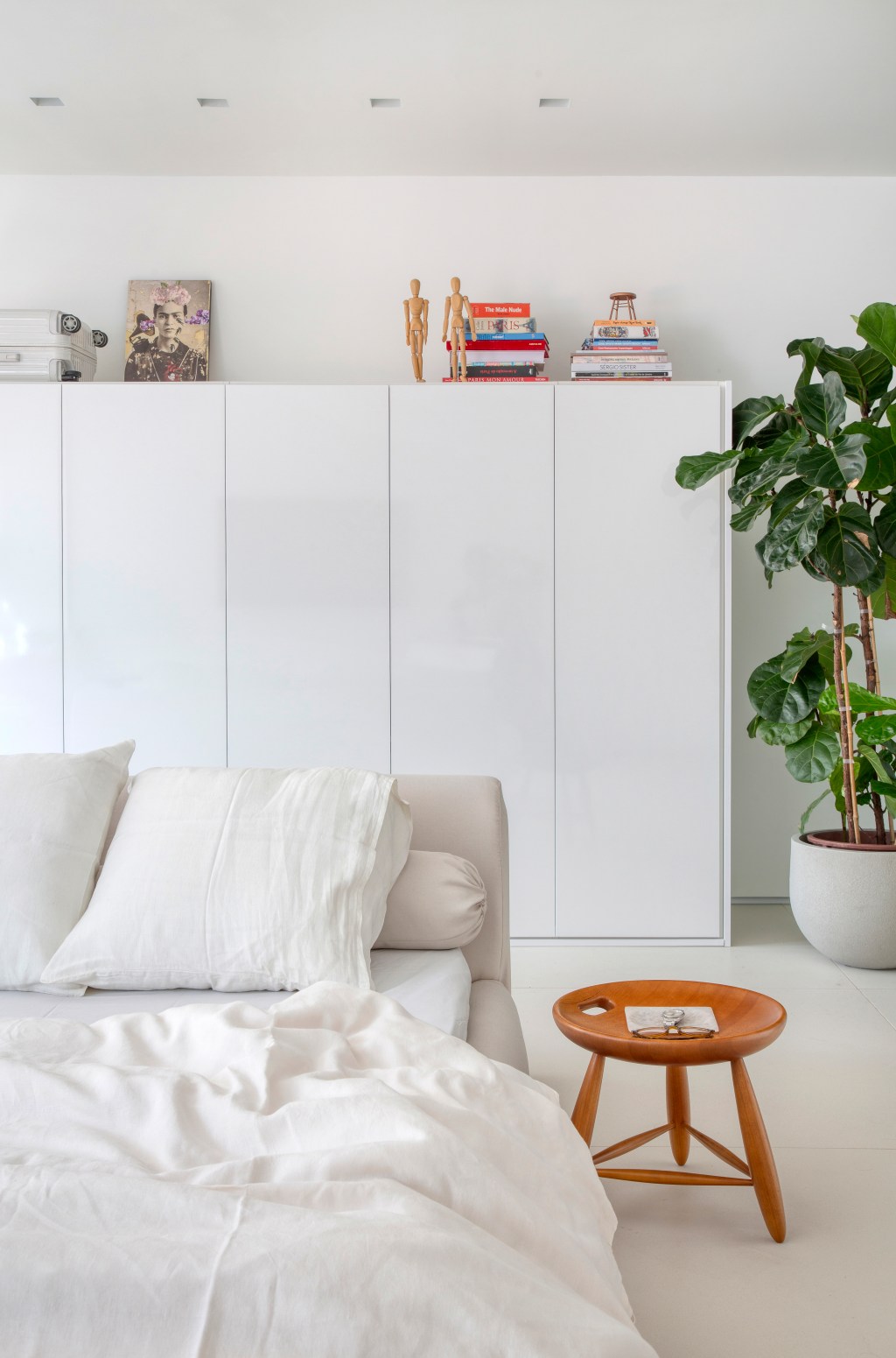 Loft de 40 m² ganha projeto minimalista que une branco e madeira. Projeto de Diego Raposo e Manuela Simas. Na foto, quarto com armário branco e vaso de plantas.
