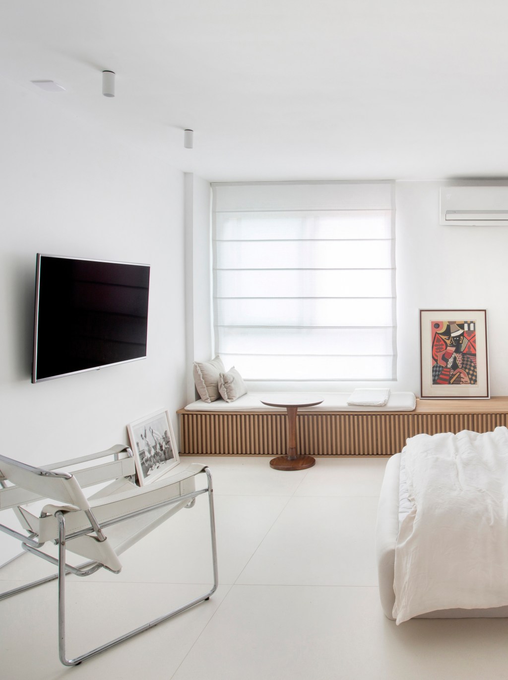 Loft de 40 m² ganha projeto minimalista que une branco e madeira. Projeto de Diego Raposo e Manuela Simas. Na foto, quarto com tv e banco ripado.
