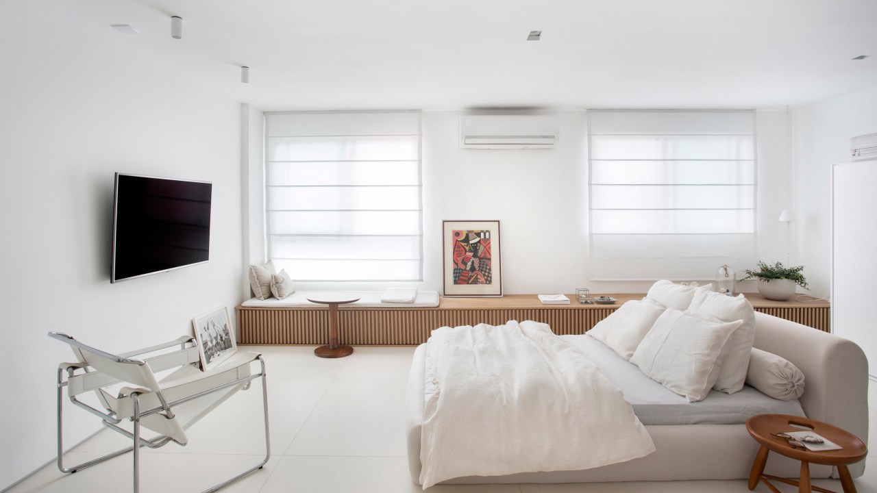 Loft de 40 m² ganha projeto minimalista que une branco e madeira. Projeto de Diego Raposo e Manuela Simas. Na foto, quarto com tv e banco ripado.