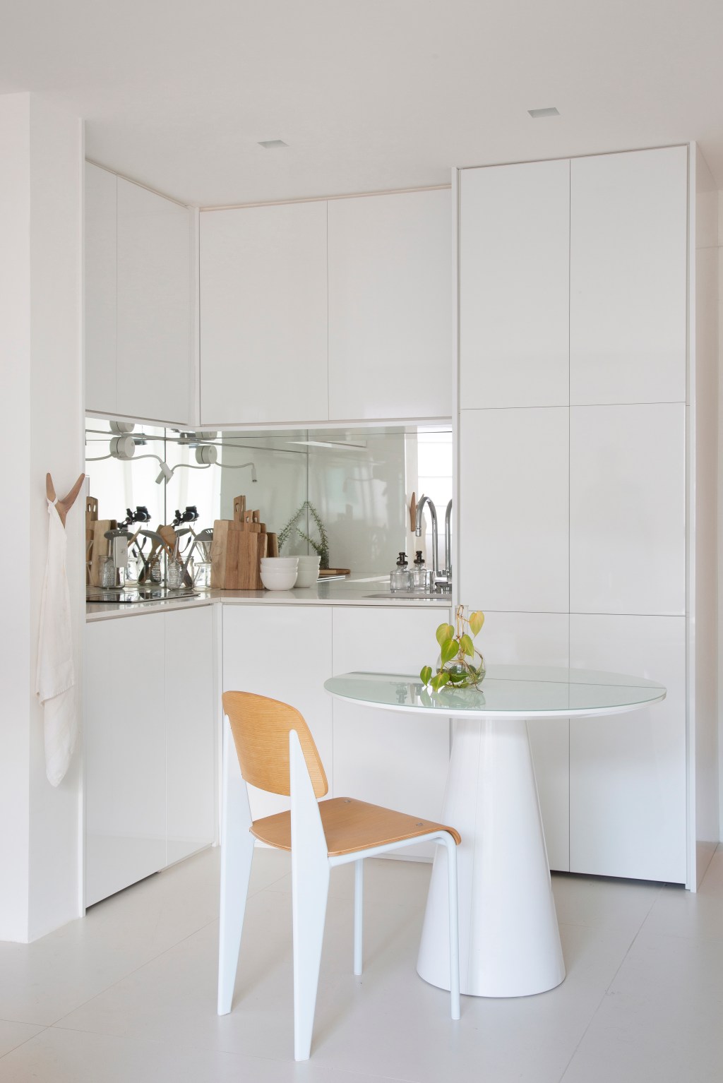 Loft de 40 m² ganha projeto minimalista que une branco e madeira. Projeto de Diego Raposo e Manuela Simas. Na foto, sala de jantar e cozinha com espelho.