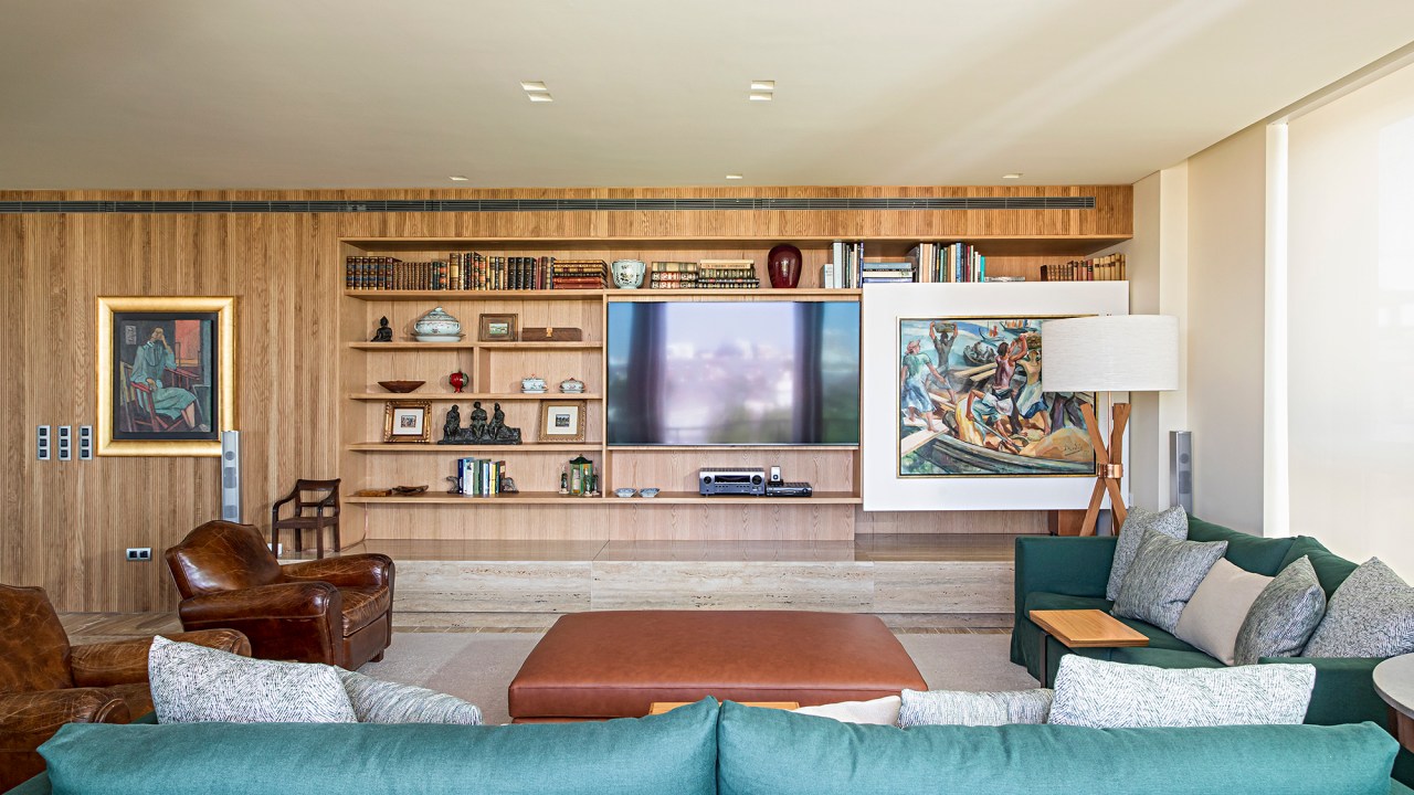Painel deslizante esconde a TV na estante neste apartamento em Portugal. Projeto de Maurício Nóbrega. Na foto, sala de estar com tv escondida e sofás verdes.
