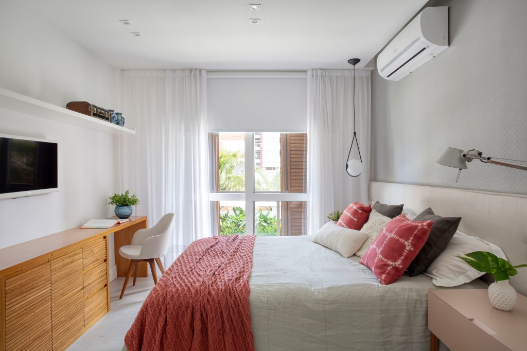 Casa de praia de 420 m² ganha estilo urbano e loft na garagem. Projeto Studio 021 Arquitetura. Na foto, quarto com cabeceira branca e colcha vermelha.