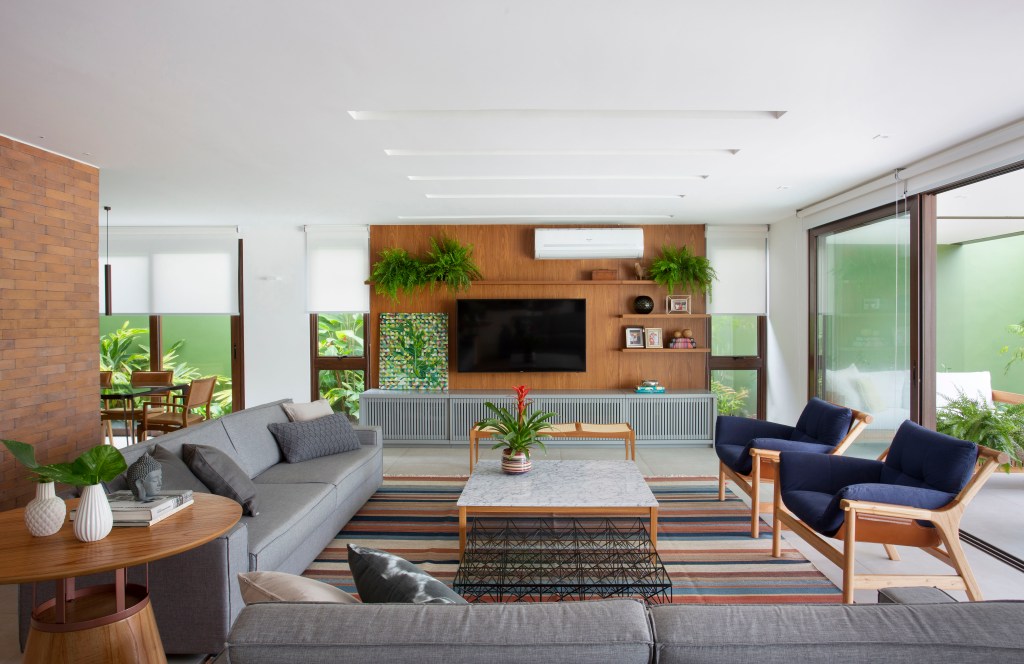 Casa de praia de 420 m² ganha estilo urbano e loft na garagem. Projeto Studio 021 Arquitetura. Na foto, sala de estar com sofá cinza e tapete listrado.
