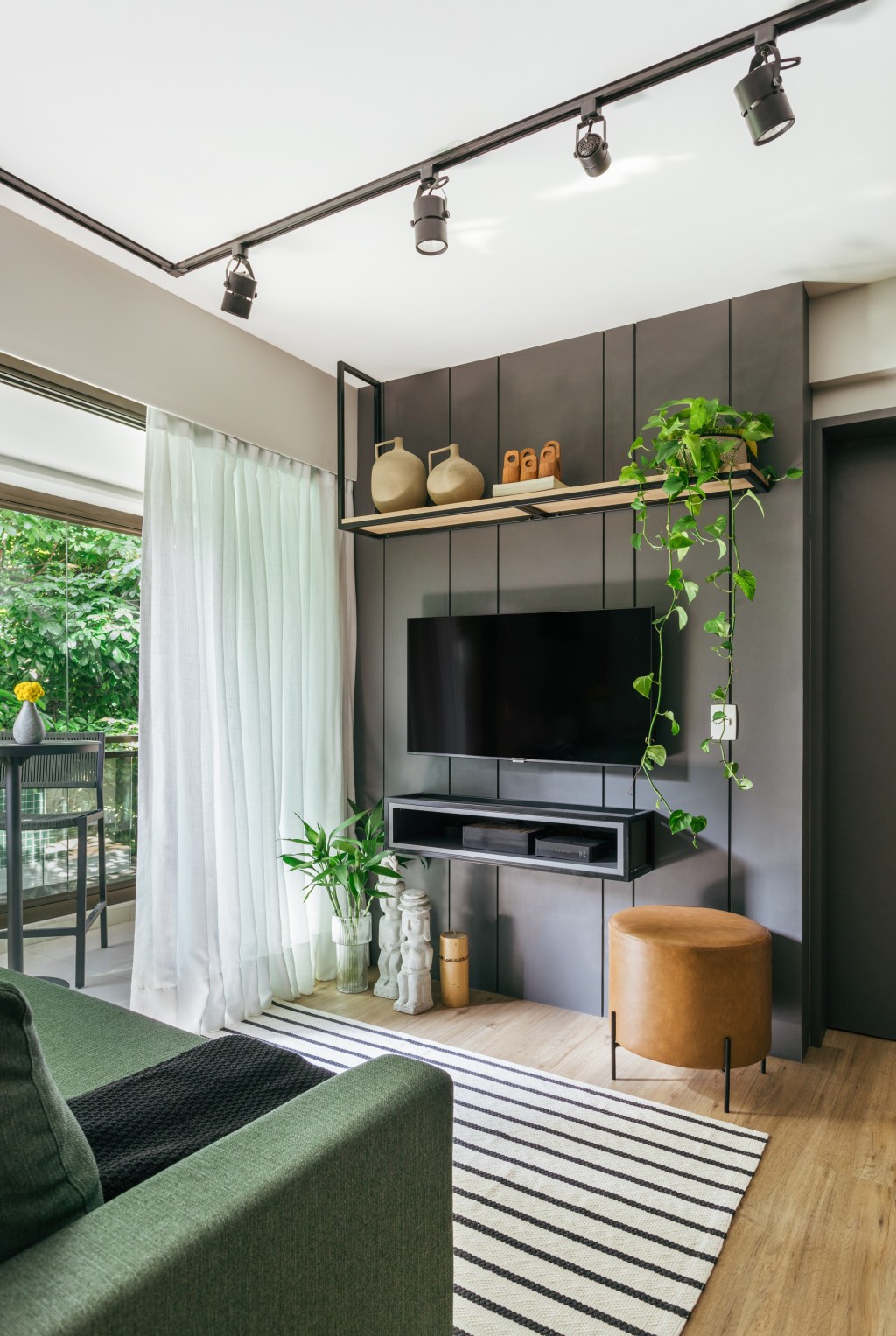 Cozinha se esconde dentro do armário neste apê de 35 m², Projeto de Ikeda Arquitetura. Na foto, sala de estar com bancada de serralheria, cozinha camuflada e sofá verde.