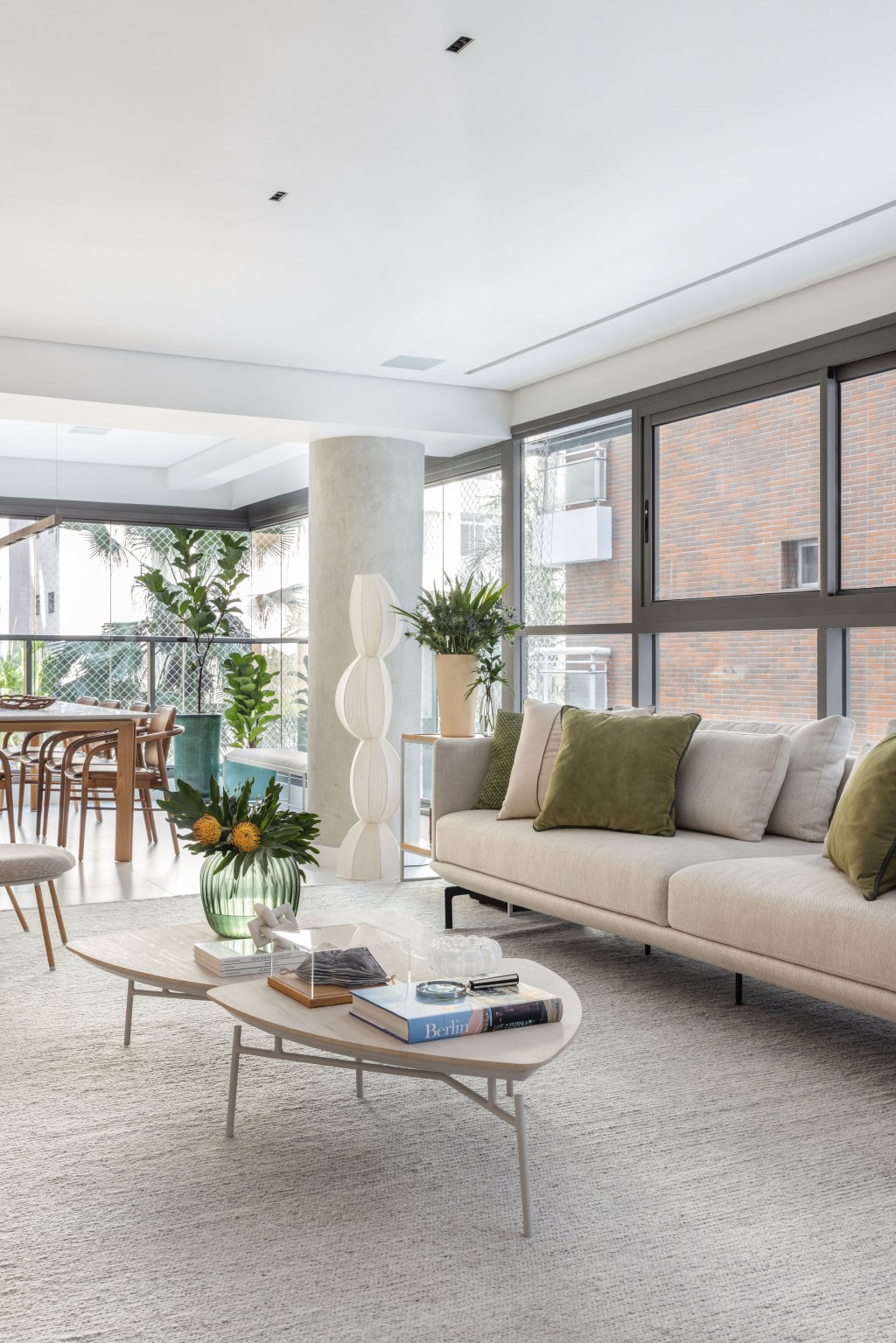 Décor neutro e ambientes integrados e fluidos marcam apartamento de 140 m². Projeto de Paula Muller. Na foto, sala de estar com sofá branco, varanda integrada e paredes de vidro.