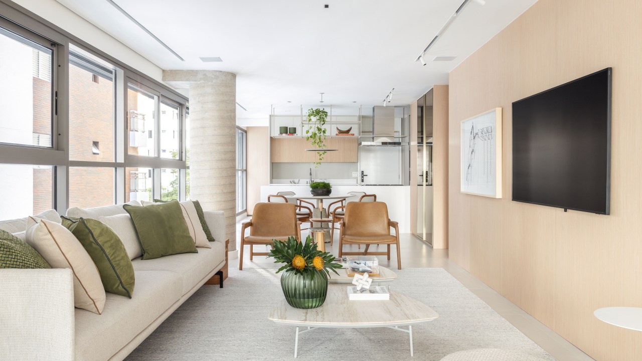 Décor neutro e ambientes integrados e fluidos marcam apartamento de 140 m². Projeto de Paula Muller. Na foto, sala de estar com sofá branco, varanda integrada e paredes de vidro.