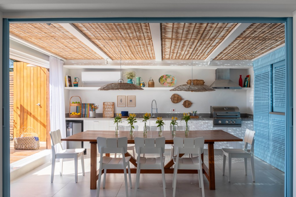 Venezianas azuis na varanda marcam esta casa de praia inspirada na Grécia. Projeto de Brise Arquitetura. Na foto, cozinha gourmet com teto de palha e vista para o mar.