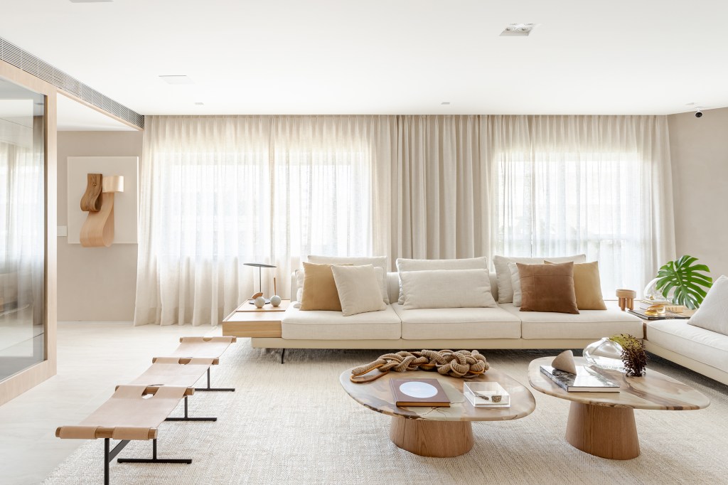 Adega walk-in e muita madeira marcam este apartamento de 300 m². Projeto de Figueiredo Fischer Arquitetos. Na foto, sala de estar com sofá em L, cortinas, mesas de centro e banco.