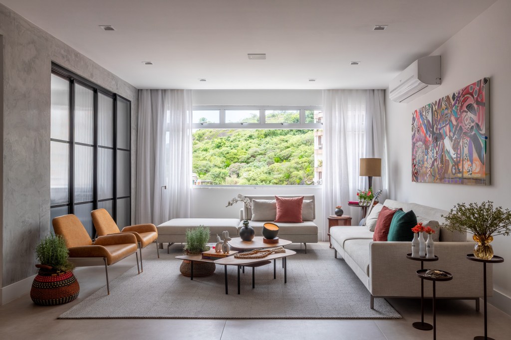 Apê industrial de 200 m² une cores, vidro canelado, tijolos e sofá jeans. Projeto de Ana Cano. Na foto, sala de estar com vista para a natureza, tapete , chaise e sofá.