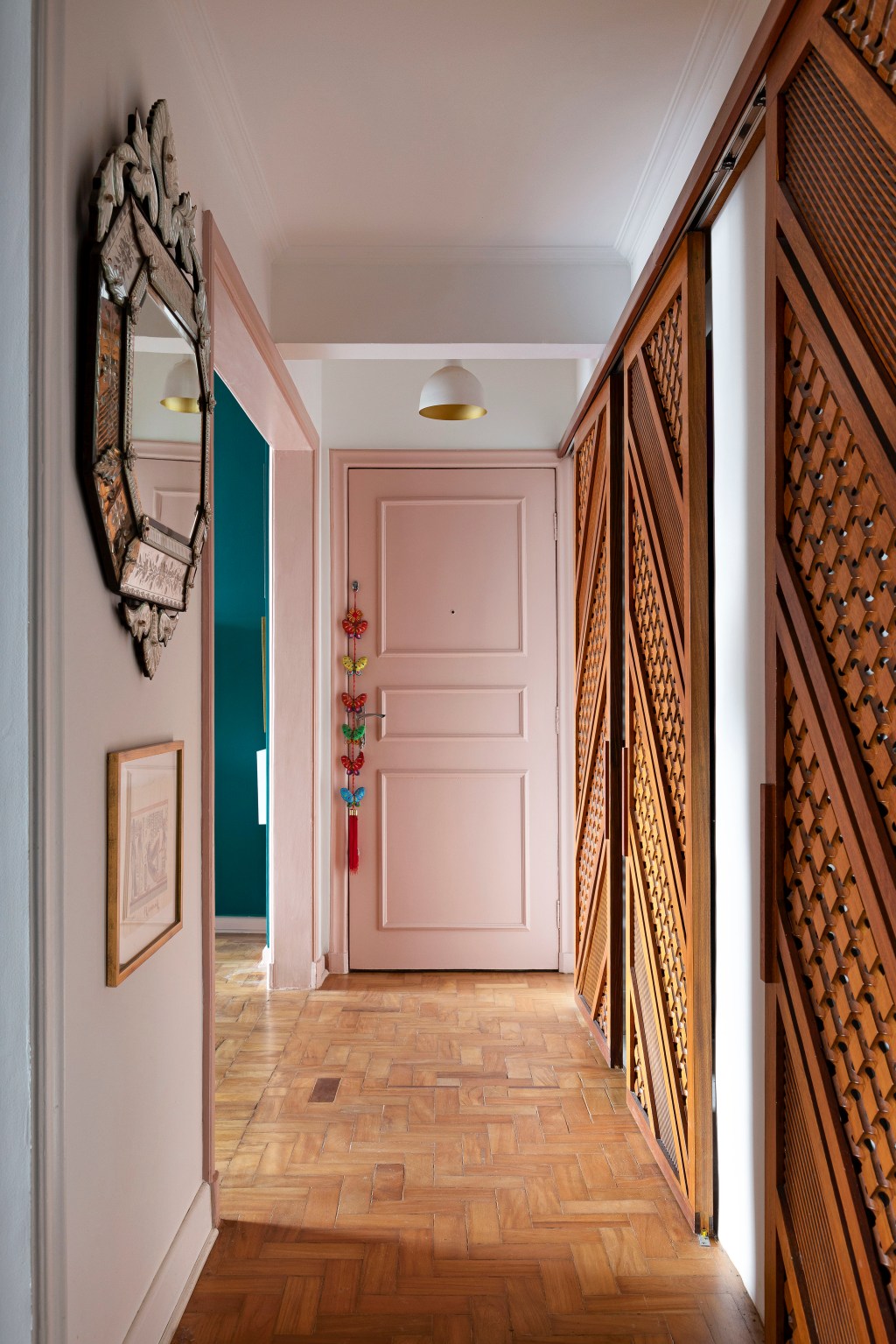 Apê de 120 m² em edifício icônico de São Paulo é repleto de cor e estampas. Projeto de Pílula Antropofágik Arquitetura. Na foto, corredor com porta rosa, esquadrias de madeira e espelho.