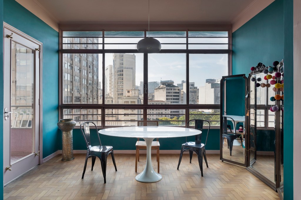Apê de 120 m² em edifício icônico de São Paulo é repleto de cor e estampas. Projeto de Pílula Antropofágik Arquitetura. Na foto, sala de jantar com mesa branca, cadeiras e espelho.