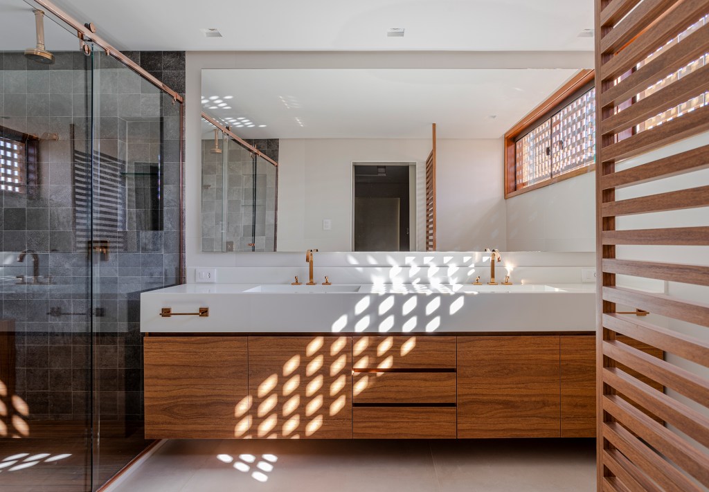 Fachada de muxarabis filtra o sol nesta casa de 430 m² na Bahia. Projeto de Sidney Quintela. Na foto, banheiro com pia dupla e parede de pedra.