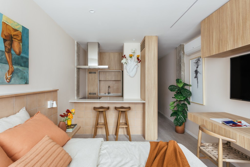 Micro apê de 25 m² tem cabeceira de azulejos e cozinha integrada ao quarto. Projeto de Rodolfo Consoli. Na foto, quarto com Tv e home office. Cozinha com balcão integrada.