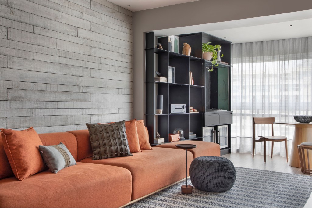 Preto e terracota marcam o décor deste apartamento masculino de 110 m². Projeto de Up3 Arquitetura. Na foto, sala com sofá terracota, estante preta e revestimento cimentício.