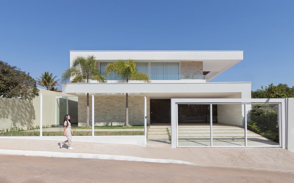Adega e escada helicoidal se destacam em casa com projeto atemporal. Projeto Traama Arquitetura. Na foto, fachada da casa com jardim.