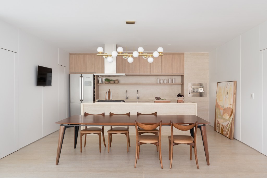 Adega e escada helicoidal se destacam em casa com projeto atemporal. Projeto Traama Arquitetura. Na foto, sala de jantar com mesa de madeira e cozinha integrada.