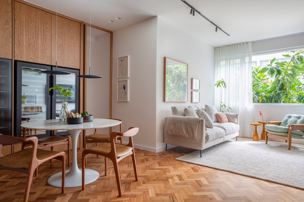 Apartamento de 110 m² ganha décor aconchegante com clima carioca. Projeto de Rafael Ramos. Na foto, sala de estar com aparador ripado e quartos. Sala de jantar com adega e mesa redonda.
