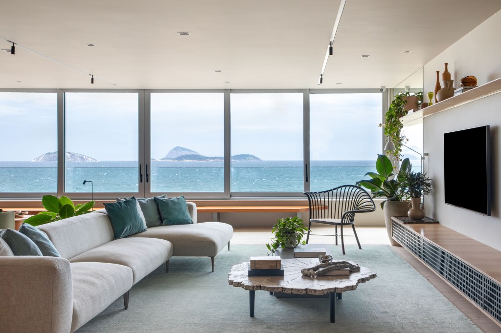 Apartamento com vista para praia ganha espaço de coworking na sala. Projeto de Up3 Arquitetura. Na foto, sala com vista para o mar, aparador e plantas.