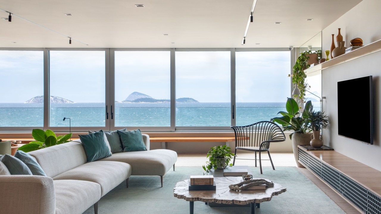 Apartamento com vista para praia ganha espaço de coworking na sala. Projeto de Up3 Arquitetura. Na foto, sala com vista para o mar, aparador e plantas.
