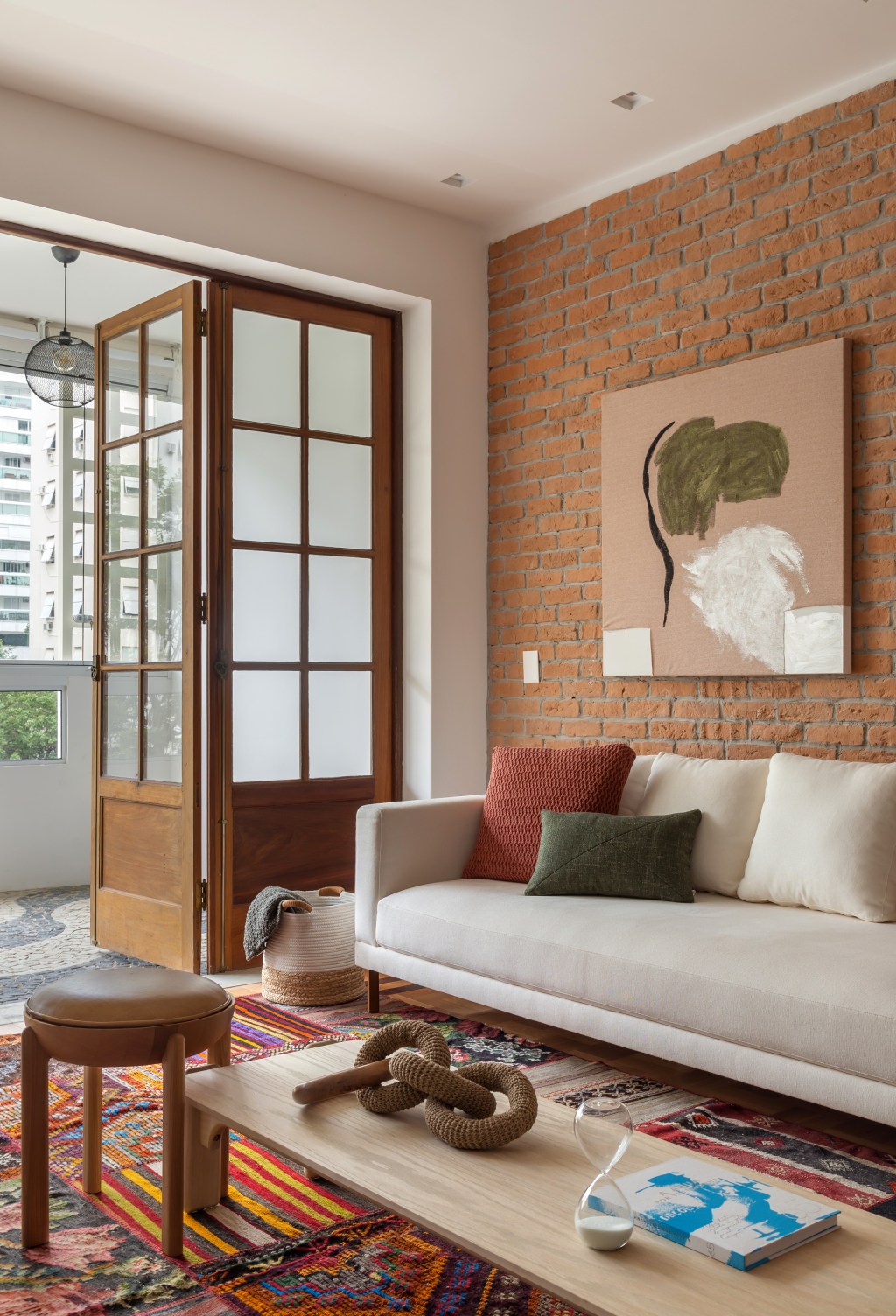 Apê de 145 m² ganha charme com tijolinhos, ladrilho hidráulico e patchwork. Na foto, sala com parede de tijolinhos, tapete de patchwork e aparador.