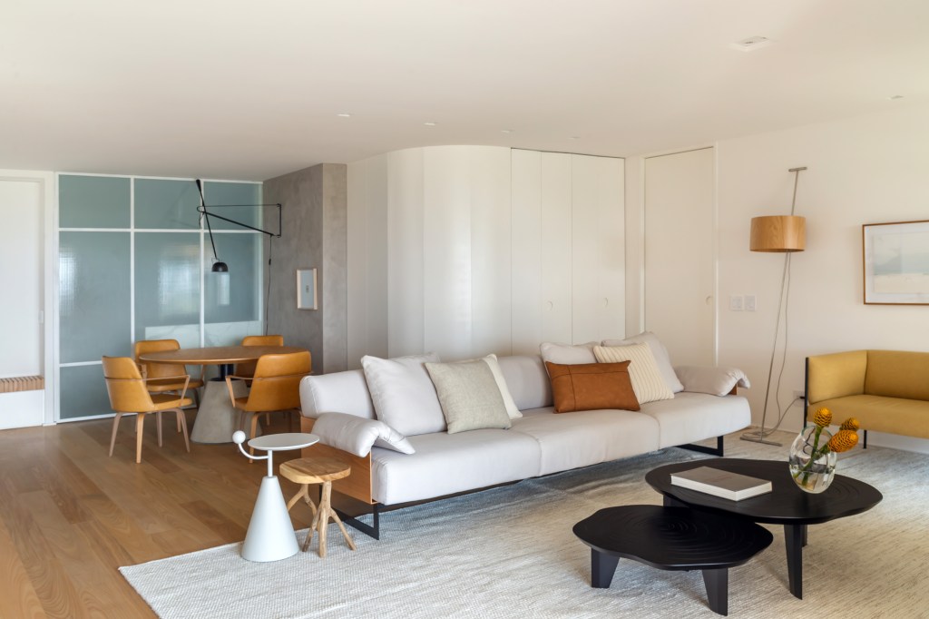 Apê na Barra da Tijuca ganha décor minimalista, mas muito aconchegante. Projeto de A+G Arquitetura, Na foto, sala com sofás, mesa de refeições e cozinha integrada.