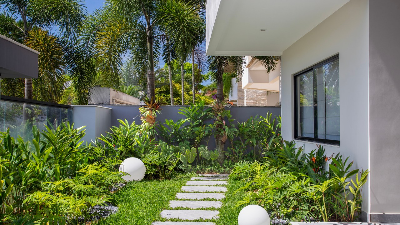 Área de 360 m² ganha jardim com paisagismo tropical e muitas flores. Projeto Maira Duarte. Na foto, jardim com espécies tropicais e luminárias esféricas.