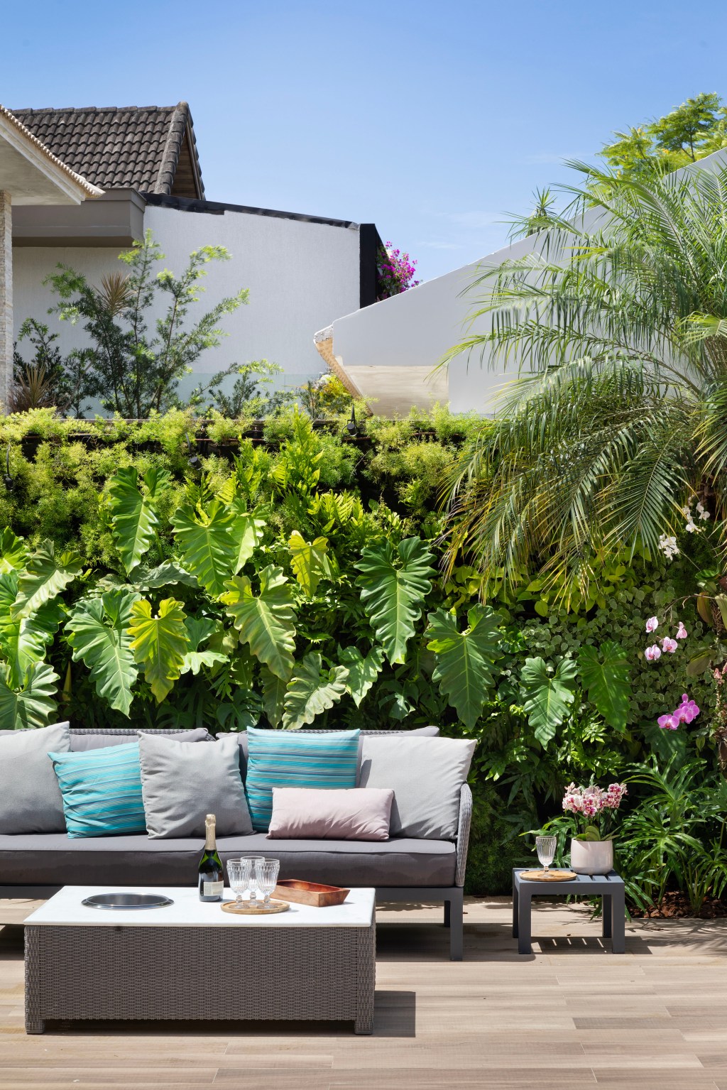 Área de 360 m² ganha jardim com paisagismo tropical e muitas flores. Projeto Maira Duarte. Na foto, varanda com parede verde e sofá.