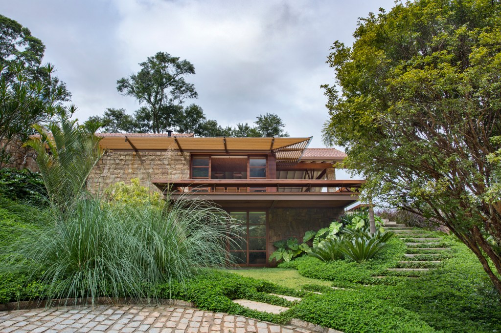 Suíte de casa de campo fica em bangalô suspenso no meio da natureza. Projeto de Escala Arquitetura. Na foto, fachada com jardim.