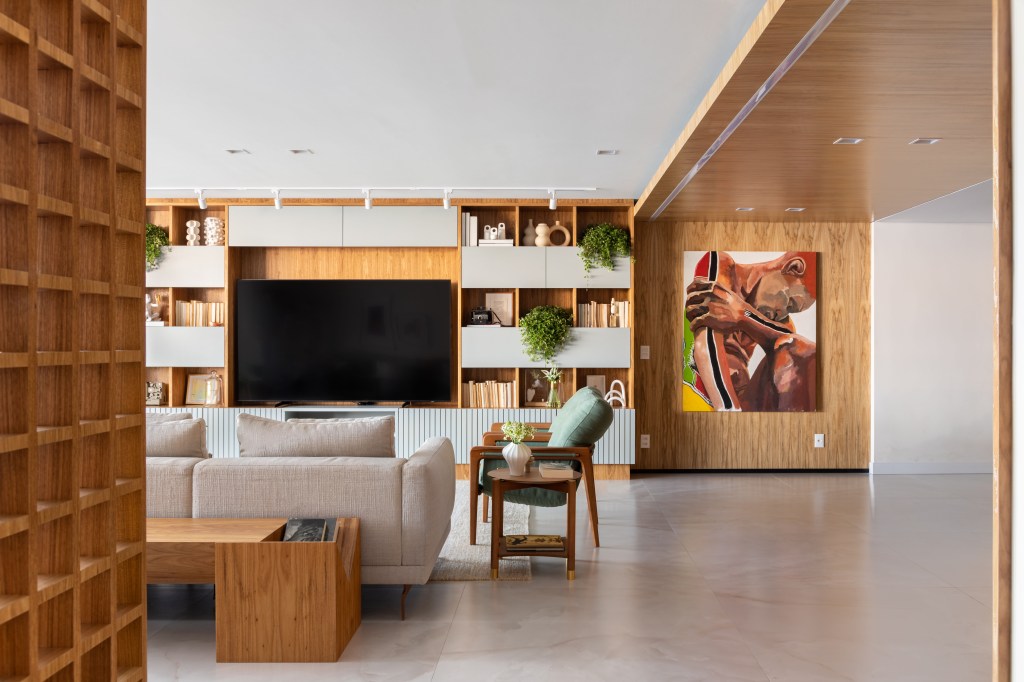 Com vista para o mar, apartamento de 270 m² exalta a arte contemporânea. Projeto de Henrique Ramalho. Na foto, sala de TV com parede de madeira e quadro.