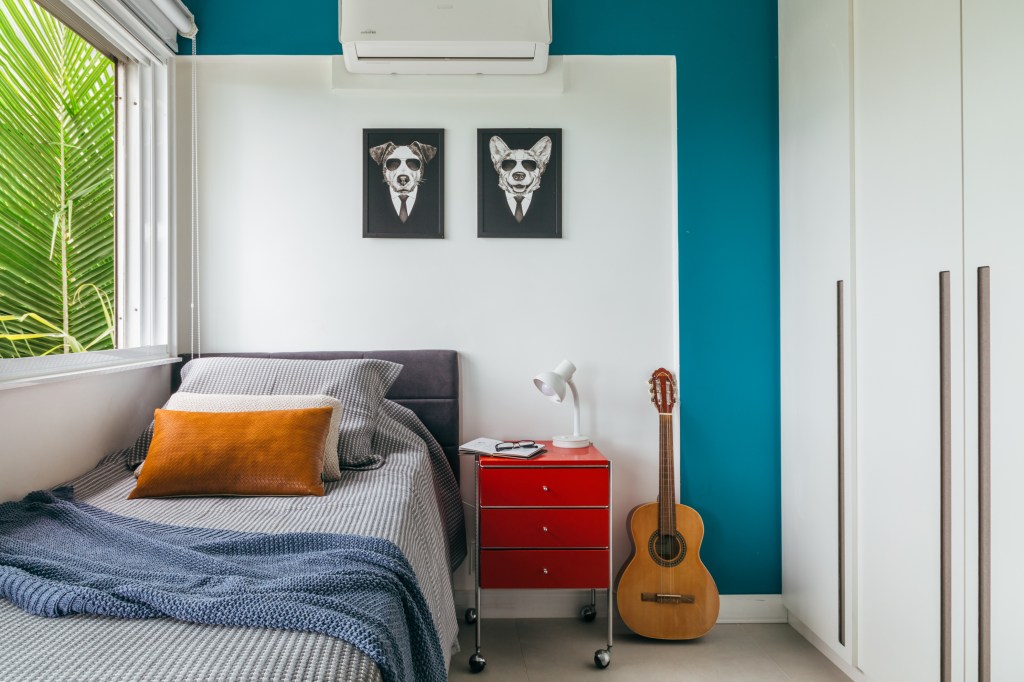 Ana Cano assina a reforma do próprio apartamento no Rio de Janeiro. Na foto. quarto com parede azul e mesa de cabeceira vermelha.