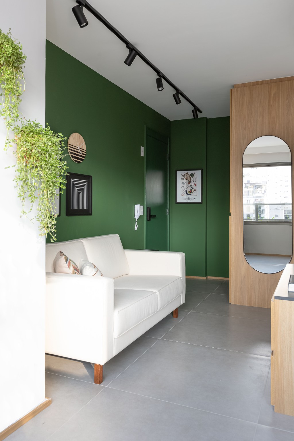 Apê de 25 m² ganha projeto jovem, integrado e funcional. Projeto de Carolina Gava, Na foto, sala com parede verde e espelho.