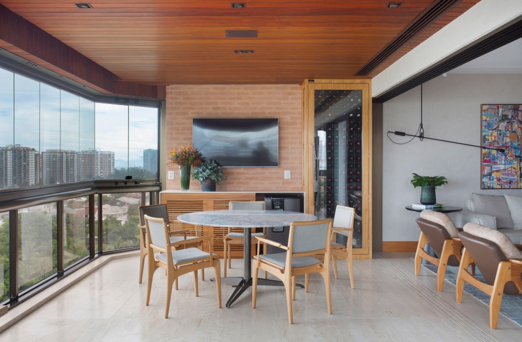 Materiais nobres e paleta atemporal marcam este apartamento de 280 m². Projeto de Studio 021. Na foto, varanda com vista para o mar e sofás. Adega e TV.