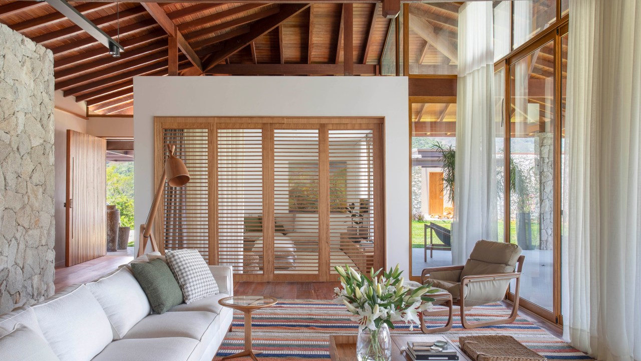 Casa de campo de 800 m² em Petrópolis ganha décor com cara de montanha. Projeto de João Panaggio. Na foto, sala com porta de madeira e poltrona.
