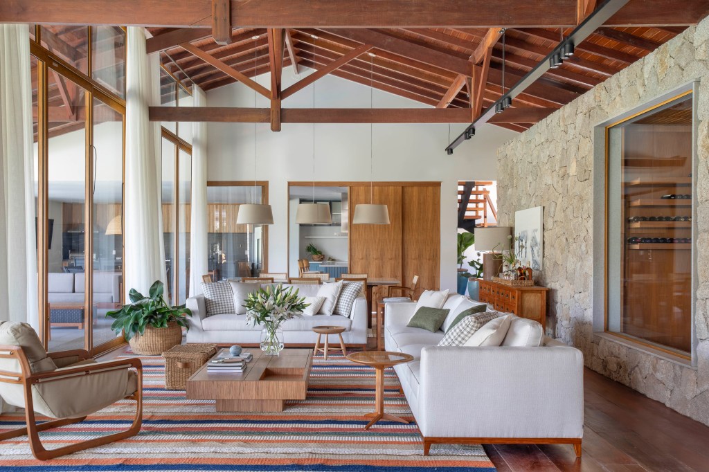 Casa de campo de 800 m² em Petrópolis ganha décor com cara de montanha. Projeto de João Panaggio. Na foto, sala com sofás. tapete e parede de pedra.