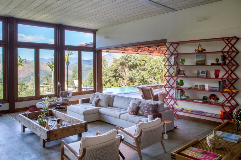 Casa na montanha possui vista espetacular para a Serra das Araras. Projeto de Andrea Chicharo. Na foto, sala de estar com vista para o jardim e estante.