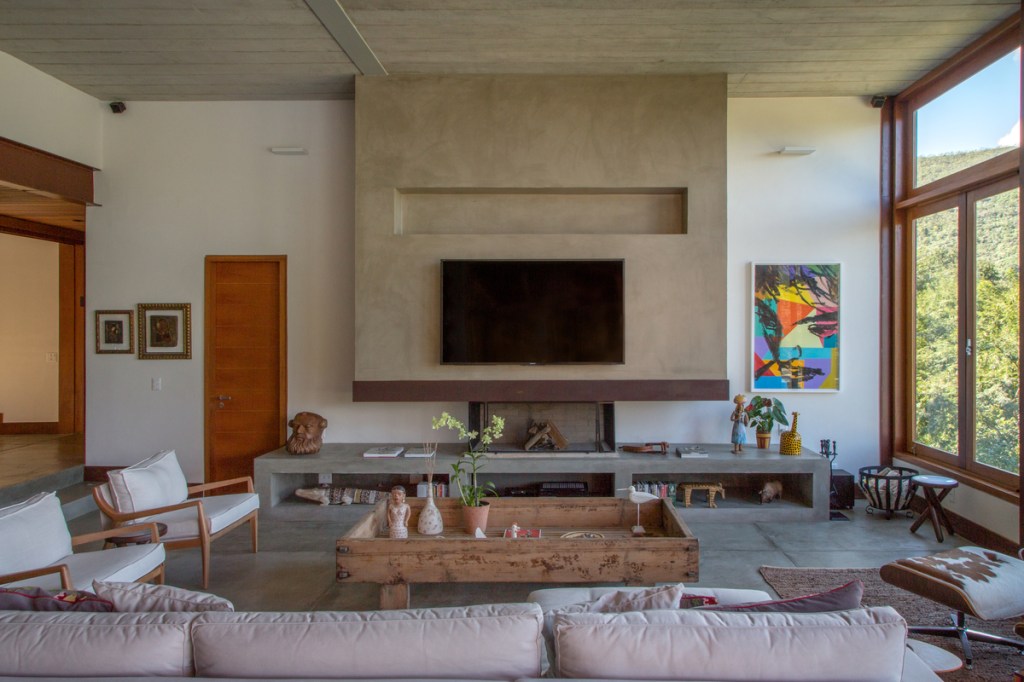 Casa na montanha possui vista espetacular para a Serra das Araras. Projeto de Andrea Chicharo. Na foto, sala de TV com lareira e aparador de concreto.