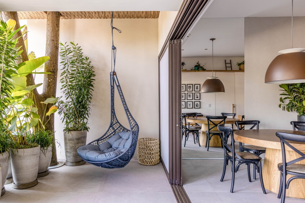 Casa no Rio de Janeiro ganha andar de lazer de 160 m² no subsolo. Projeto de Escala Arquitetura. Na foto, varanda com poltrona suspensa e mesa de jantar.