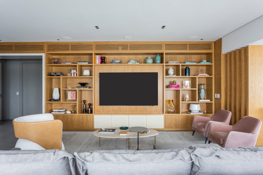 Contemporaneidade, integração e tons neutros marcam apartamento de 311 m². Projeto BZP Arquitetura. Na foto, sala de estar com estante embutida e poltronas rosas.