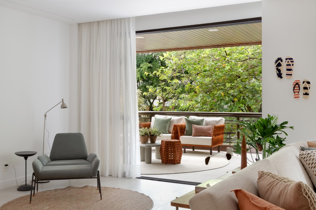 Décor neutro, tons terrosos e verde oliva marcam este apê de 230 m². Projeto de Paula Muller. Na foto, sala com varanda, vista para as árvores e poltrona.