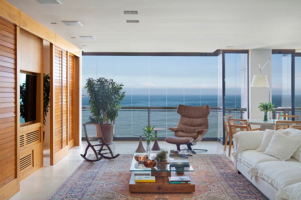 O mar do Leblon é o pano de fundo deste apartamento de 280 m². Projeto de Studio 021 Arquitetura. Na foto, sala de estar com vista para o mar e móveis brancos.